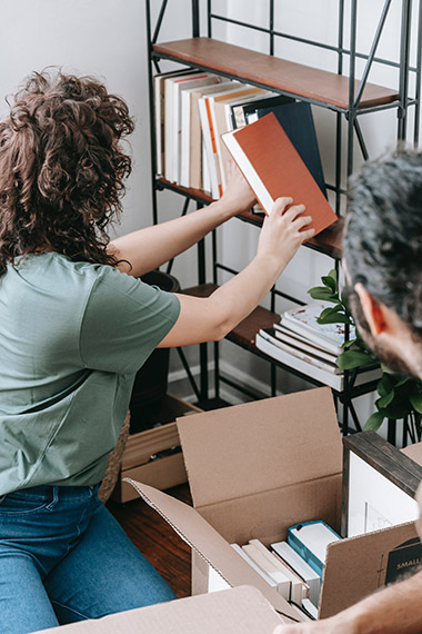 woman decluttering and packing up books on shelf