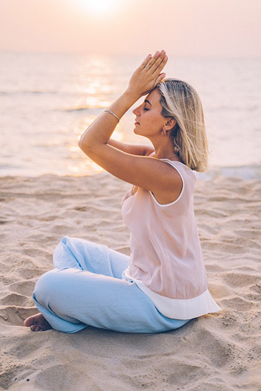woman meditating on sand at the beach