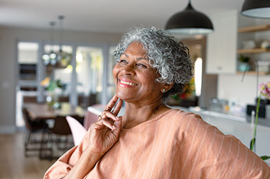 Woman smiling as she touches her face while contemplating