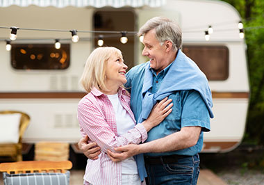 Retired couple embracing in front of their RV in a campground