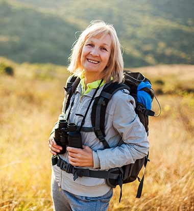 woman hiking wearing backpack, smiling and holding binoculars